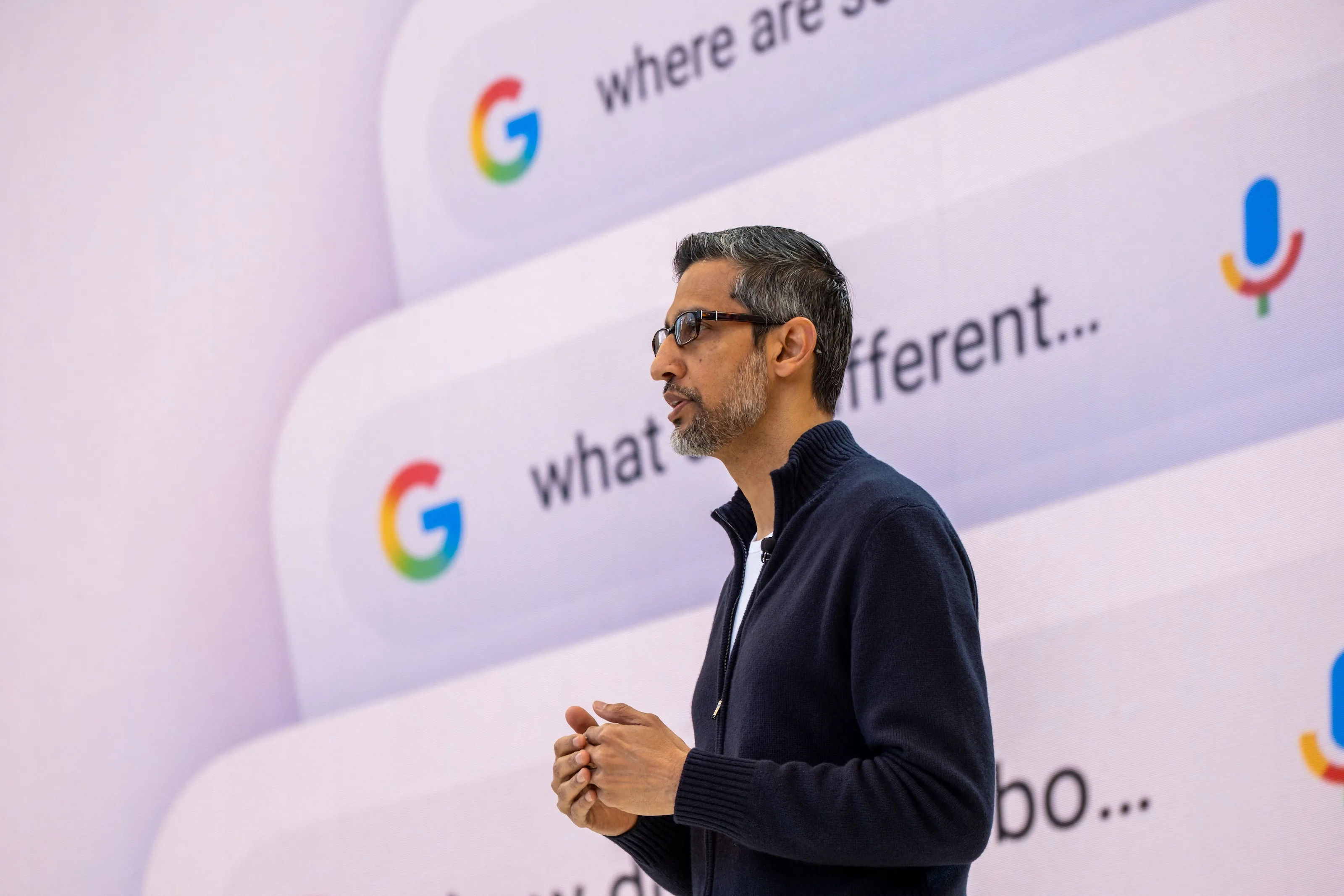 Sundar Pichai delivering the Google I/O 2026 keynote in front of an AI-powered Search backdrop showing personalised query suggestions